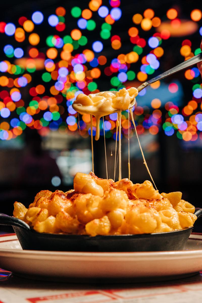 Mac n' Cheese being scooped out of a piping hot skillet.