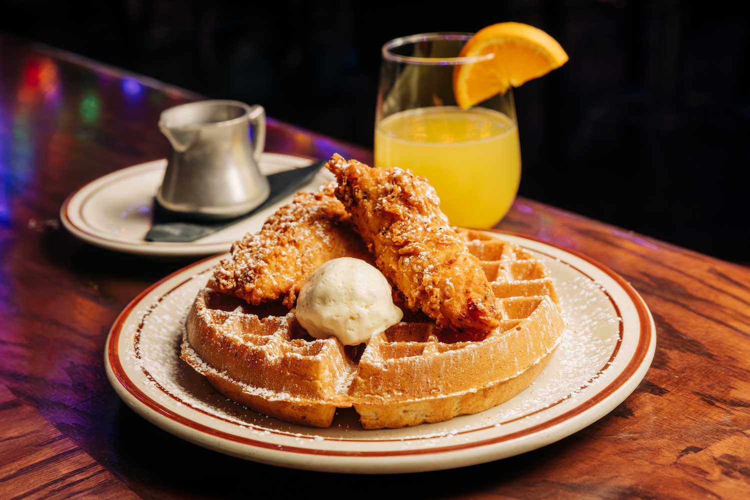 Fried chicken and waffles on a plate with syrup in the back and a mimosa behind it.
